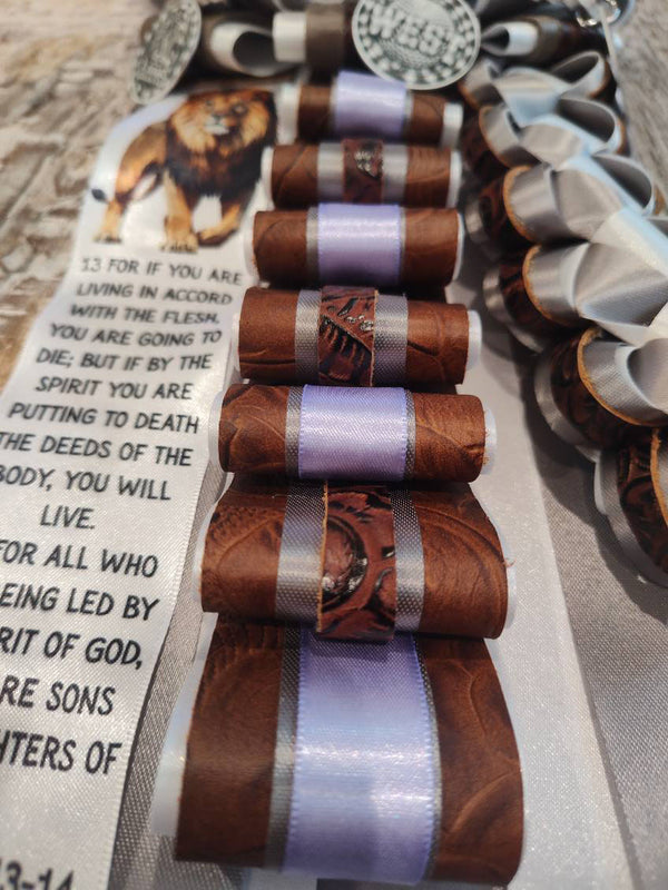Close-up of a brown and lavender homecoming garter with leather-look loops, a lion charm, and a Scripture verse ribbon
