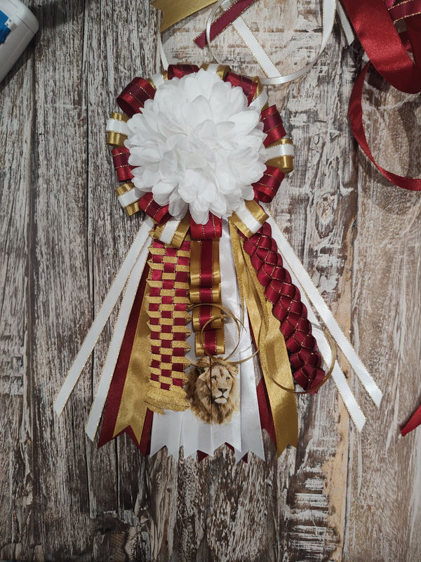 Mini homecoming mum in maroon, gold, and white with a white flower center, woven braids, and a lion charm