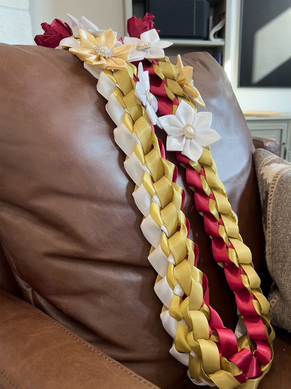 Graduation lei of braided maroon, gold, and white ribbon with satin flowers, draped over a leather chair