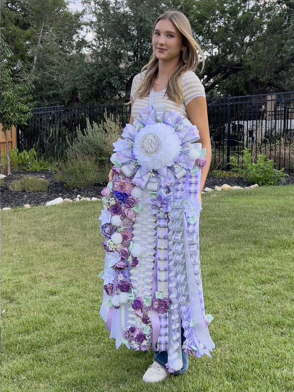Student holding a full-length lavender, white, and mint homecoming mum outdoors