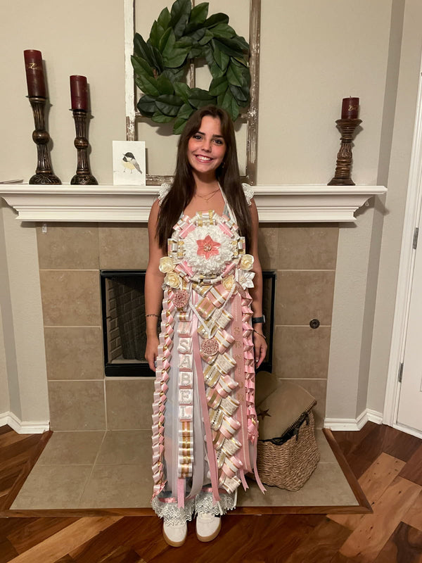 Student wearing a full-length blush pink, white, and gold homecoming mum at home