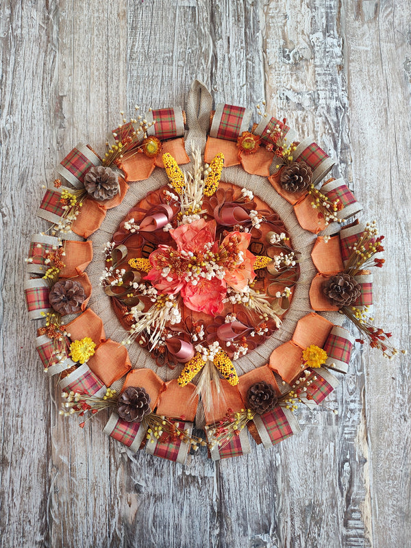 Round fall wreath with orange and plaid ribbon loops, pinecones, wheat, and dried flowers around a burlap ring