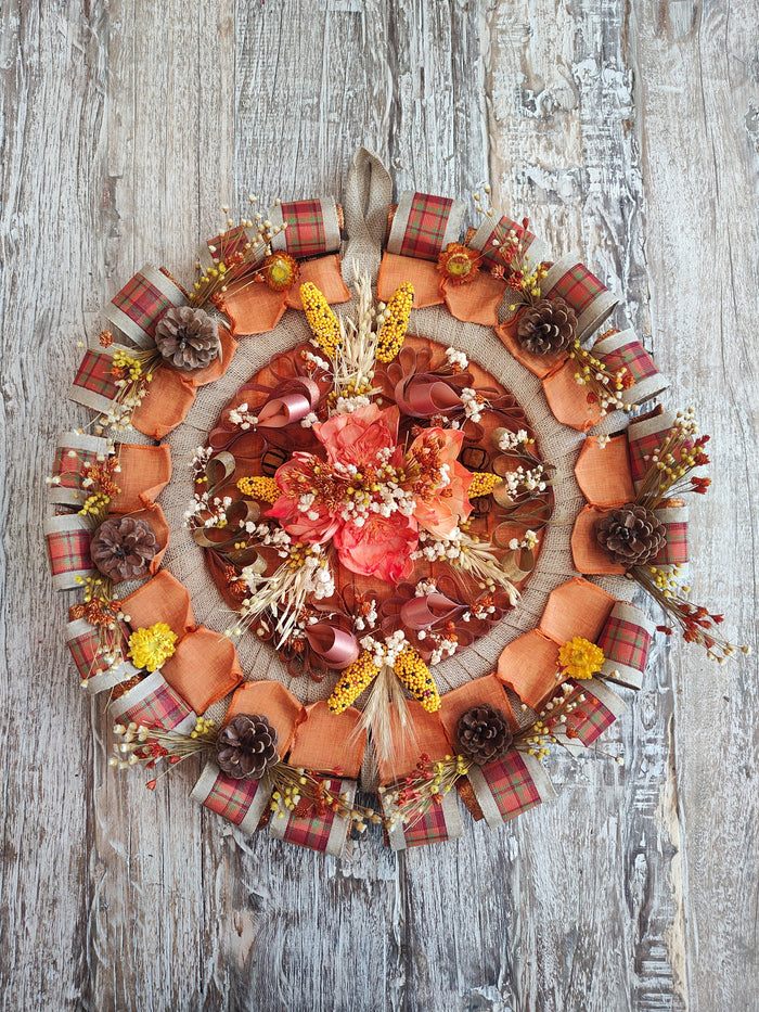 Round fall wreath with orange and plaid ribbon loops, pinecones, wheat, and dried flowers around a burlap ring