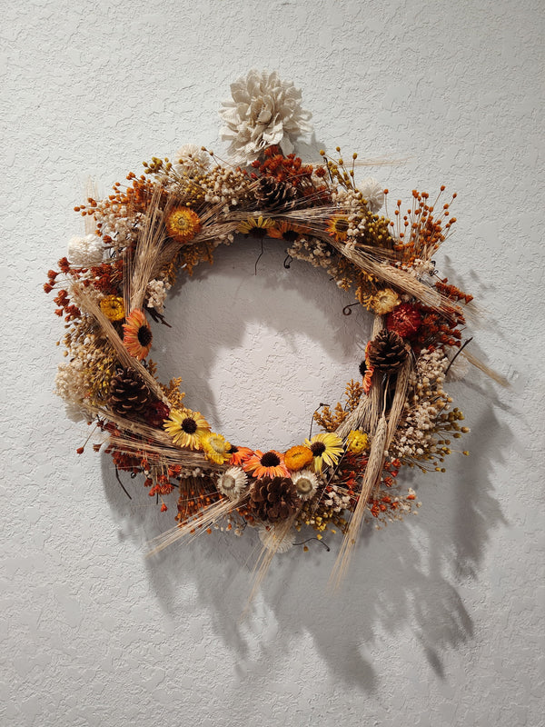 Fall wreath of wheat, sunflowers, pinecones, and dried orange and cream flowers on a twig base, hanging on a wall