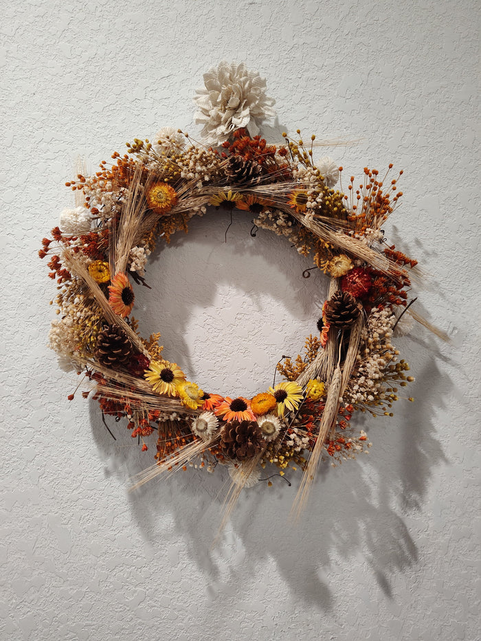 Fall wreath of wheat, sunflowers, pinecones, and dried orange and cream flowers on a twig base, hanging on a wall