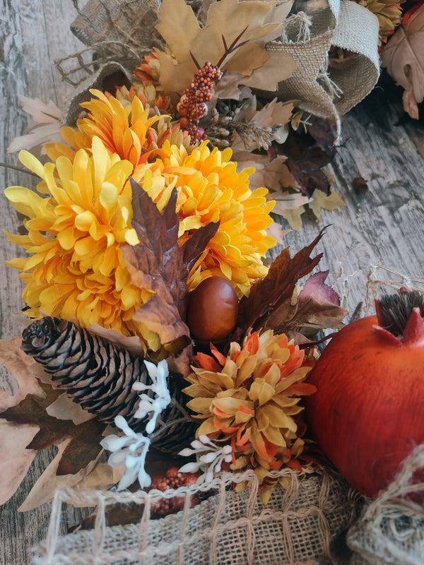 Close-up of a fall wreath with golden chrysanthemums, a pinecone, an acorn, white berry sprigs, and a red pomegranate